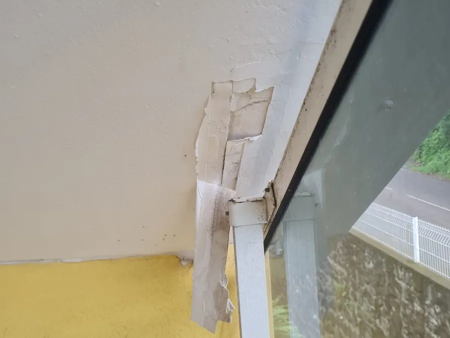 Le plafond sous un escalier extérieur, enduit décollé et plaques qui pendent au-dessus du garde-corps