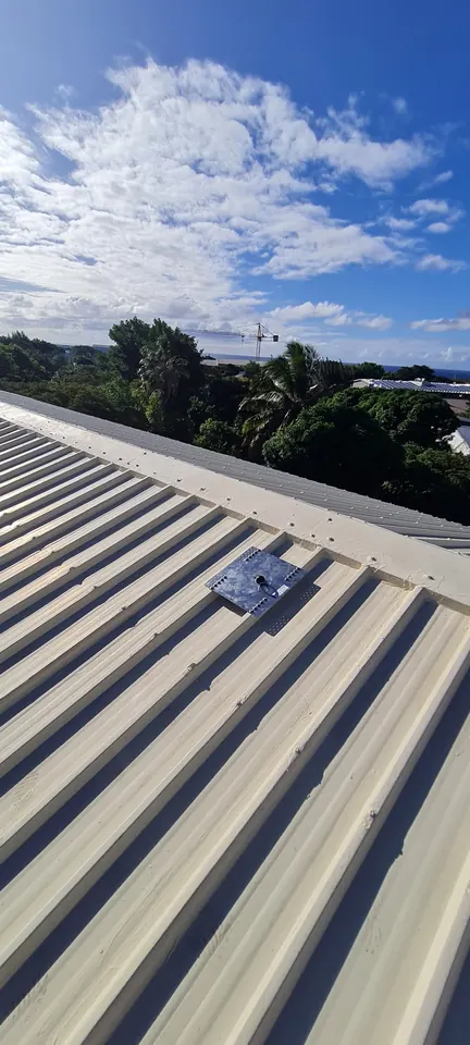 Platine d'ancrage vissée sur une toiture en bac acier, végétation et mer à l'horizon