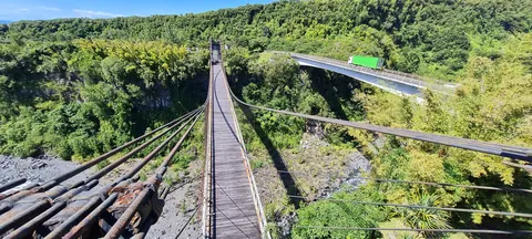 Le tablier du pont suspendu de Sainte-Rose vu depuis un pylône, la ravine et le pont routier à droite