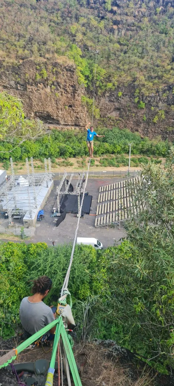 Slackline tendue au-dessus d'un site d'événement en contrebas d'une falaise, un marcheur au milieu