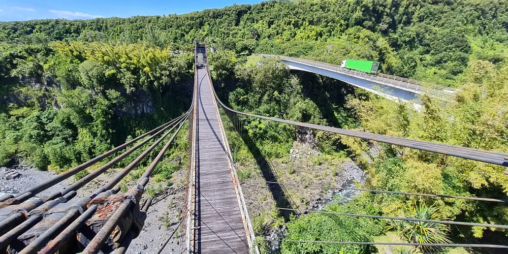 Le tablier du pont suspendu de Sainte-Rose vu depuis un pylône, la ravine et le pont routier à droite